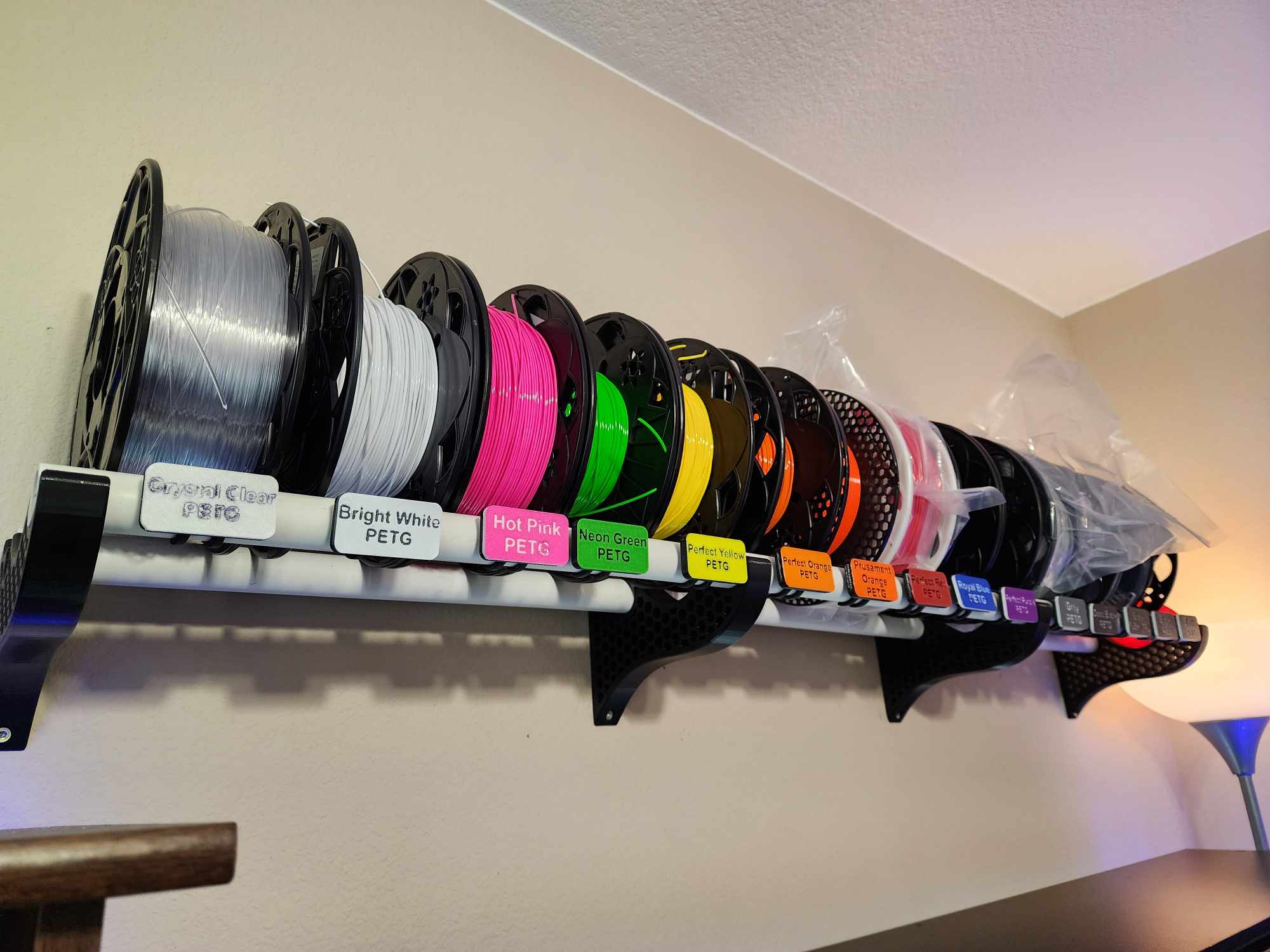 3D printed filament shelf brackets holding spool-storage pipe on a maker shelf