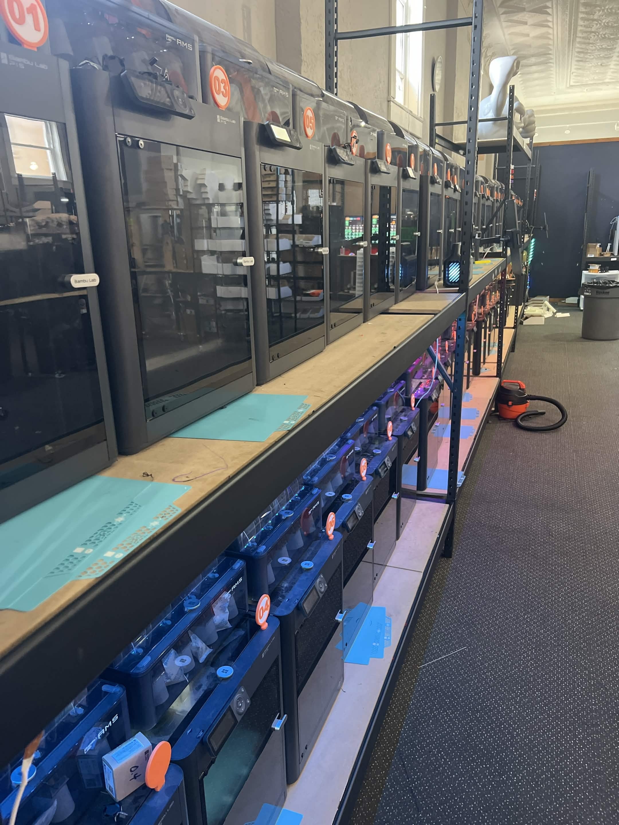 Inside the GoodPrints3D print farm with rows of enclosed 3D printers running on shelving, showing real production capacity for prototype and small-batch work.