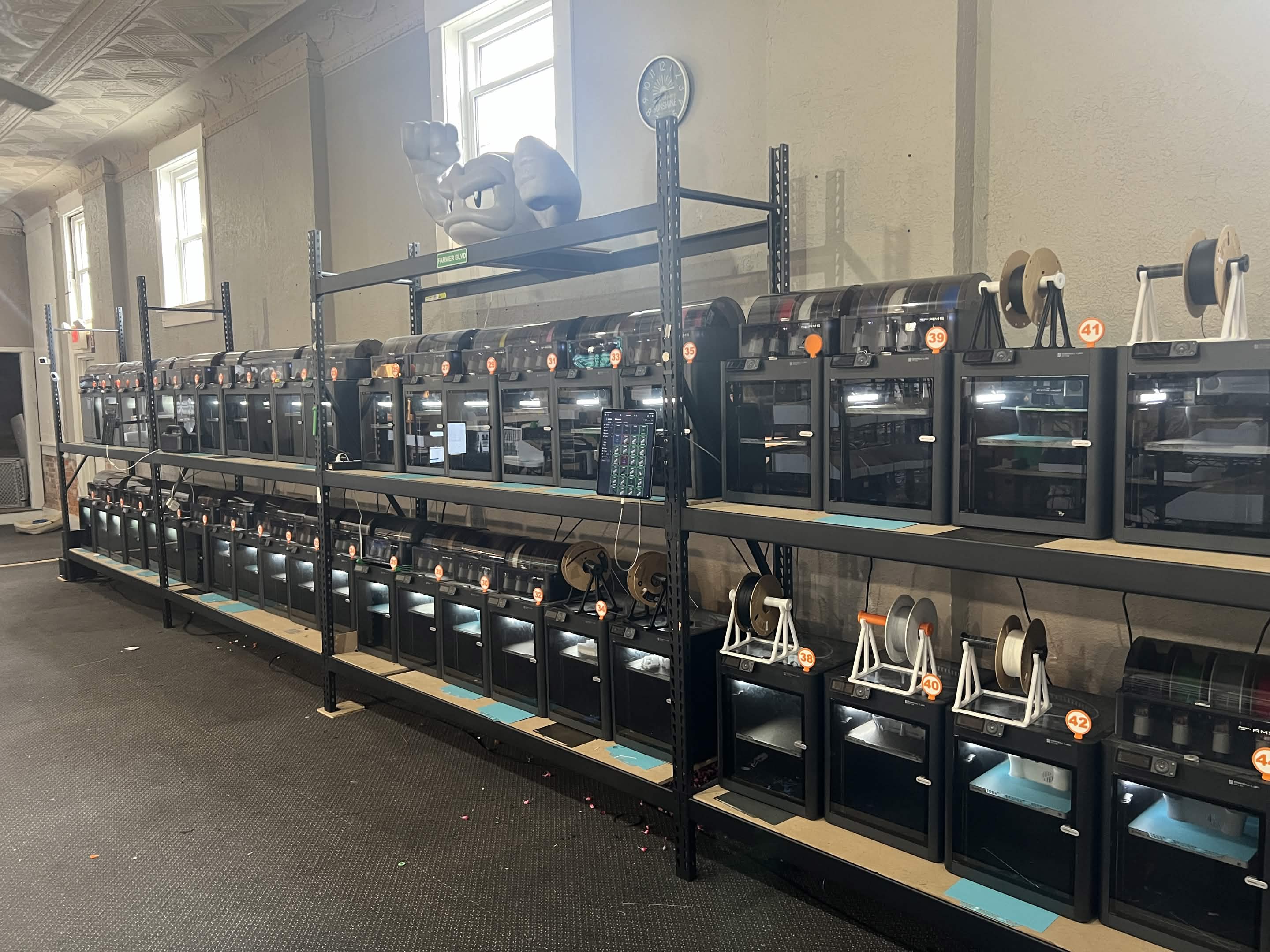 Wide view of the GoodPrints3D printer farm with many numbered enclosed printers in production, supporting repeatability and controlled reorder workflows.