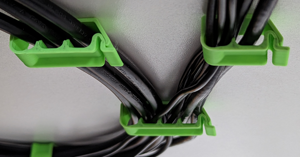3D printed KLAMMA locking cable clips mounted under a desk to keep everyday cables in reach