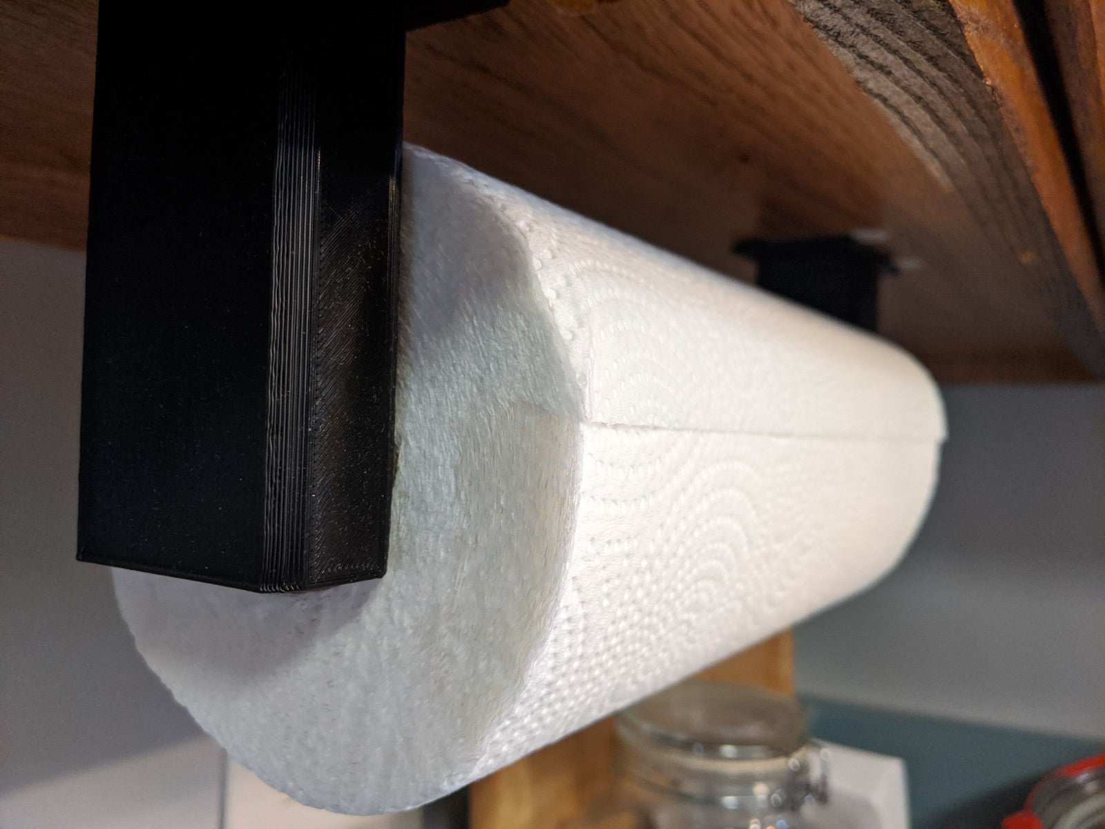 Under-cabinet 3D printed paper towel holder mounted beneath a cabinet with a paper towel roll installed