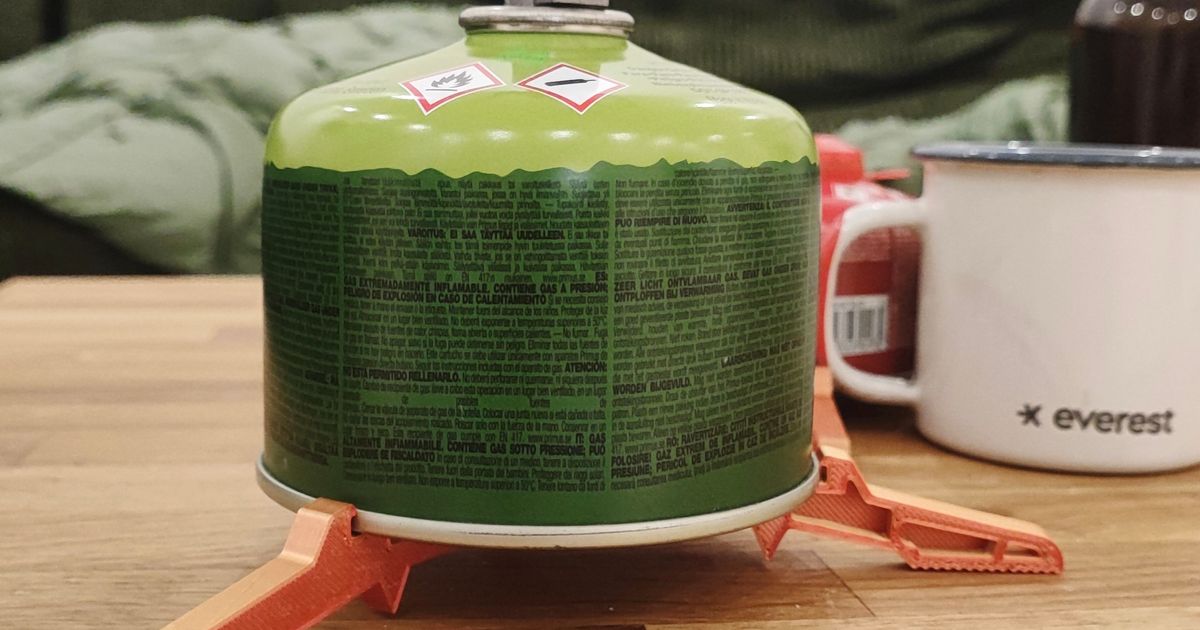 3D printed camping gas canister stand supporting a small stove fuel canister on an outdoor surface