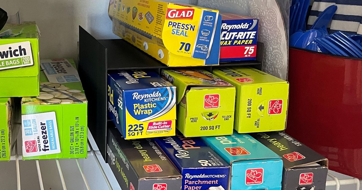 3D printed pantry organizer holding foil, parchment paper, wax paper, and plastic wrap boxes upright in a cabinet